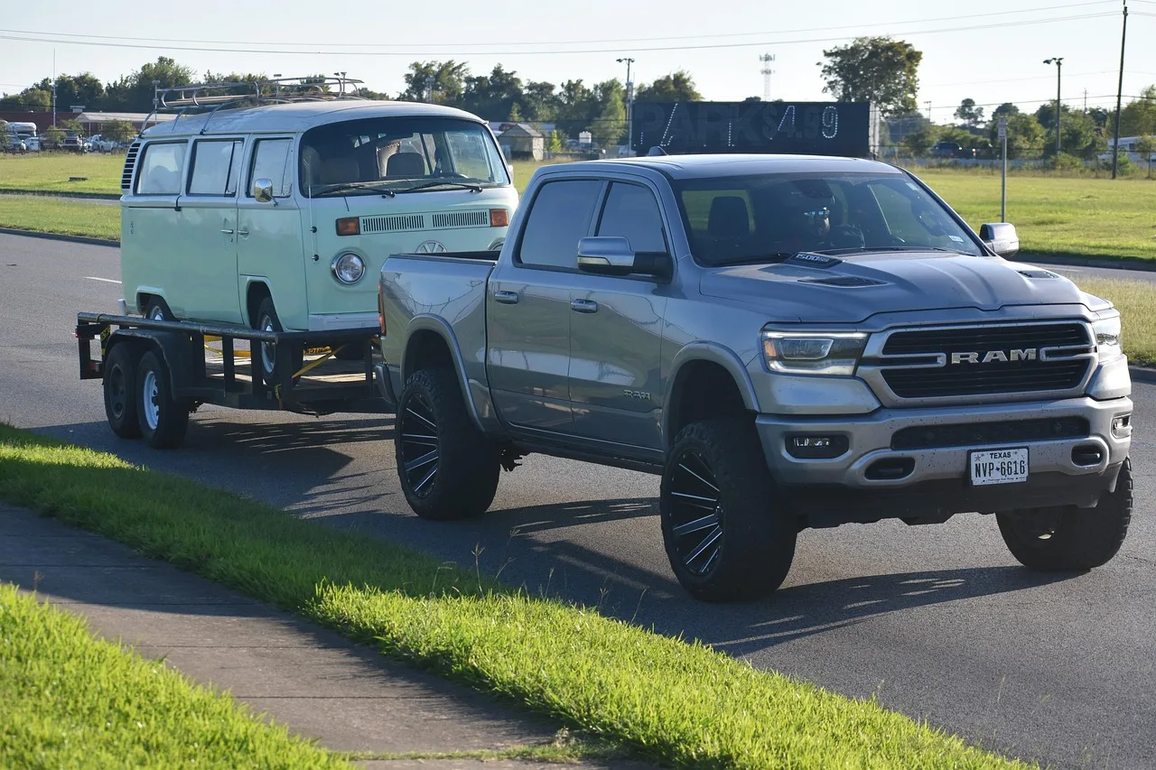 RAM pickup truck backing and towing a Volkswagen van on a flatbed trailer — practicing low-speed maneuvering builds confidence