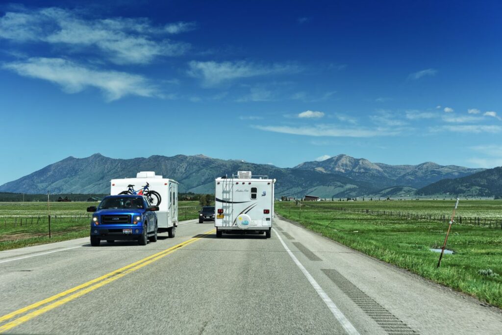 Confident driver in a blue pickup truck towing a camper through mountain scenery